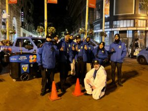 A group of people in uniforms at night posing in front of Union Square branded vehicles.