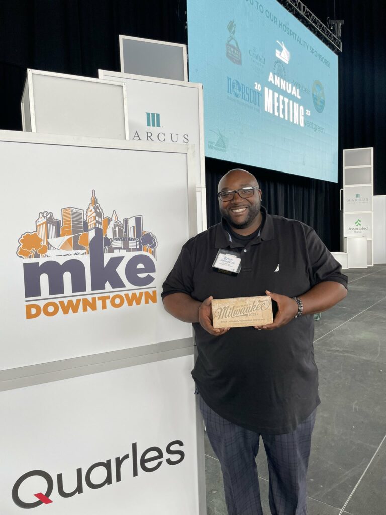 Brian Johnson holds his Heart of Milwaukee award next to a sign.