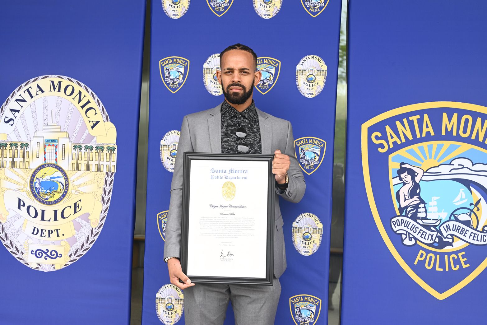 A man in a suit holds an award in front of a Santa Monica Police Department logo.