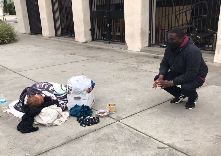 An Outreach Worker squats to check on a sleeping street resident.