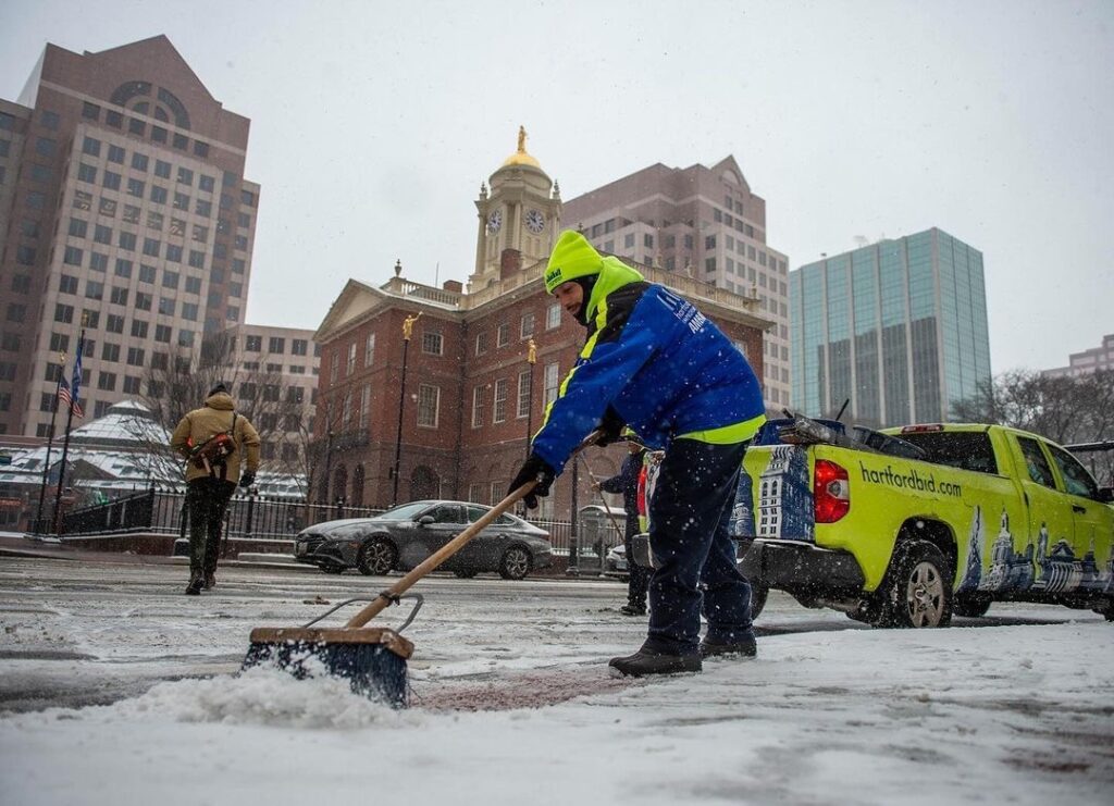 An MDID Ambassadors brushes snow off a sidewalk.
