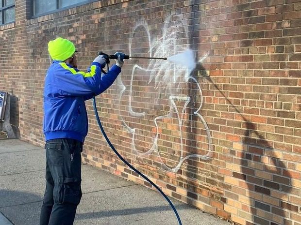 An Ambassador pressure washes graffiti on a brick wall.