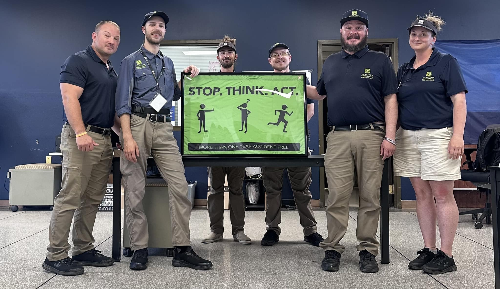 A group of uniformed Ambassadors stand by a framed Green flag.